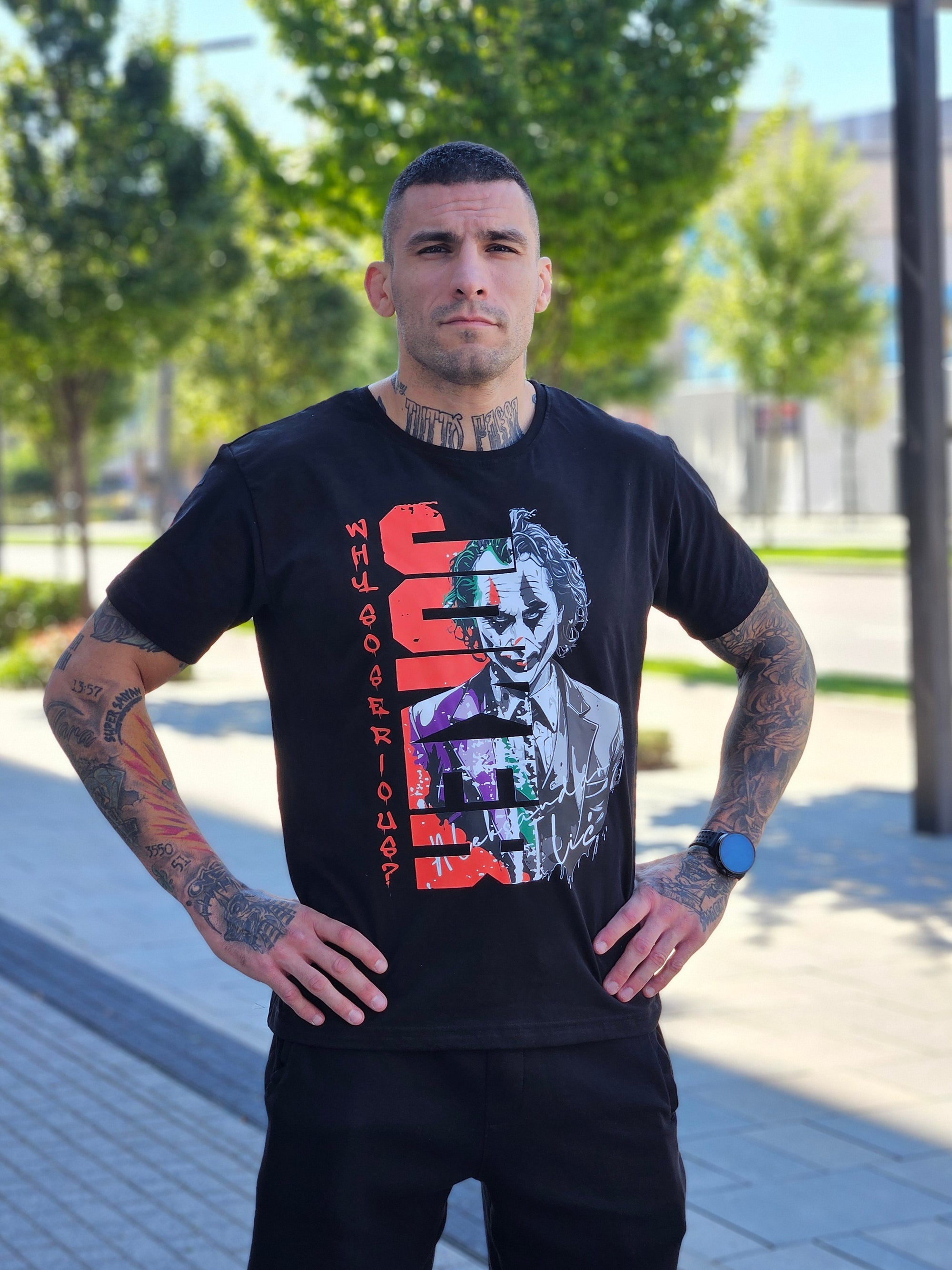 Man wearing a black t-shirt with colorful graphics and text, standing outdoors.